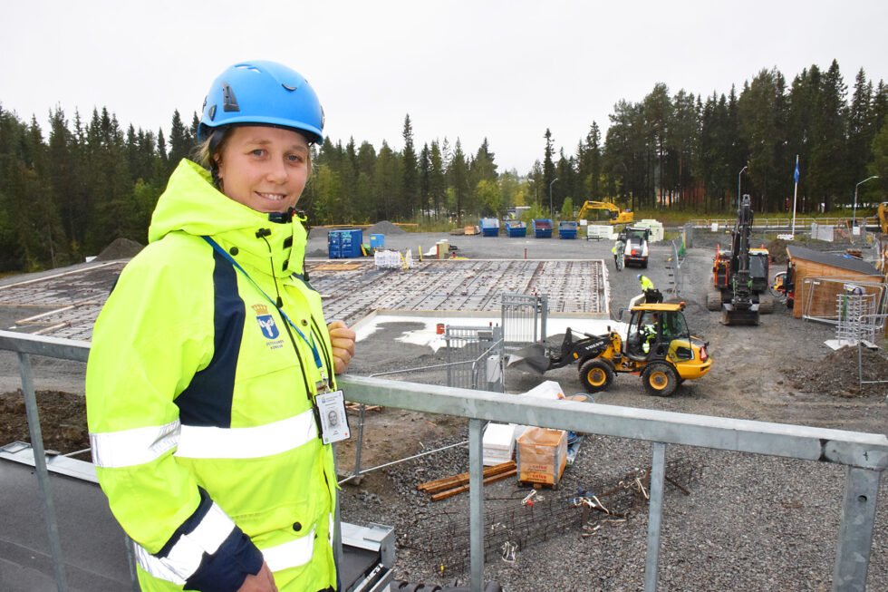 kvinna i bygghjälm och varselkläder vid en byggarbetsplats där markarbeten pågår