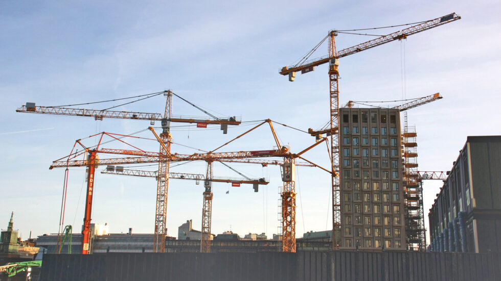 I kartläggningen som Svensk Byggtjänst genomfört framgår att många efterlyser en tydligare ansvarsfördelning och vägledningar inför införandet av de nya byggreglerna. Fotot visar en byggarbetsplats med flera kranar och ett flervåningshus som håller på att byggas.