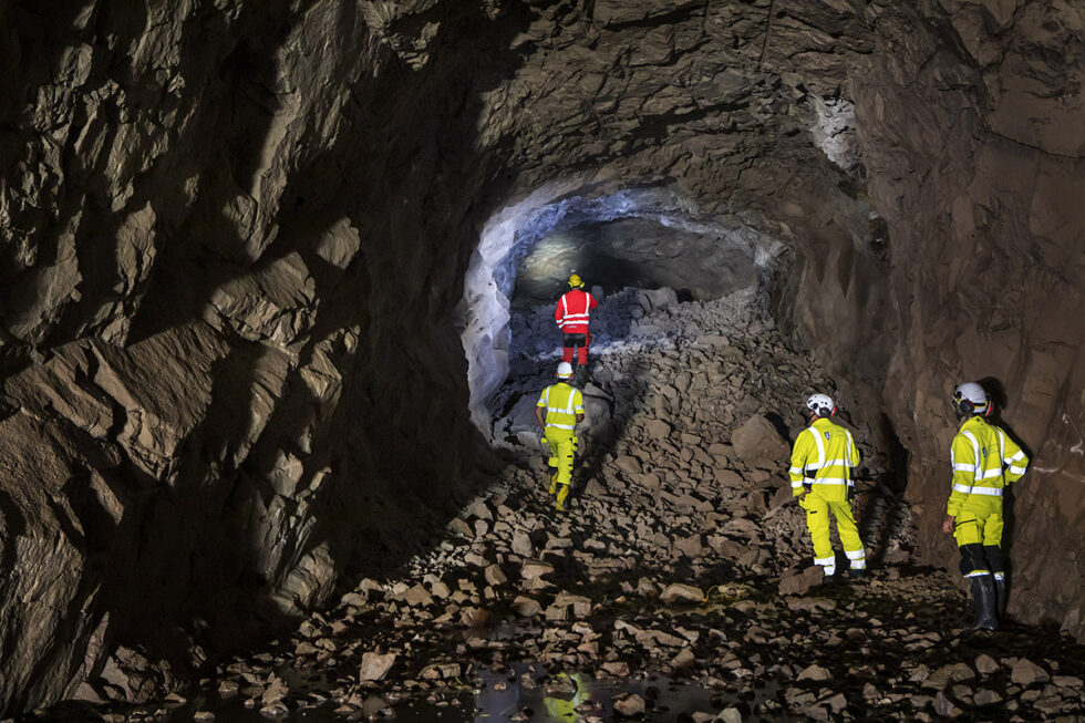 Genombrott i avloppstunneln under Bromma. Fyra personer i arbetskläder vid tunnelöppningen.