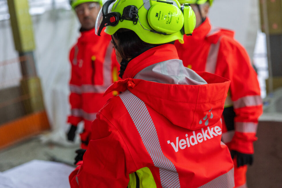 Orange varseljacka med Veidekkes nya logotyp över ryggen.