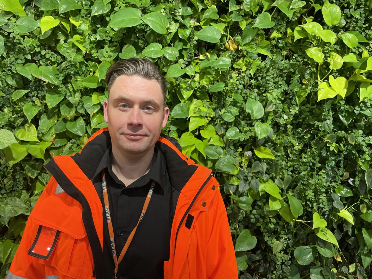 Fredrik Jihammar, regionchef på Peab, i varseljacka framför en grönskande vägg.